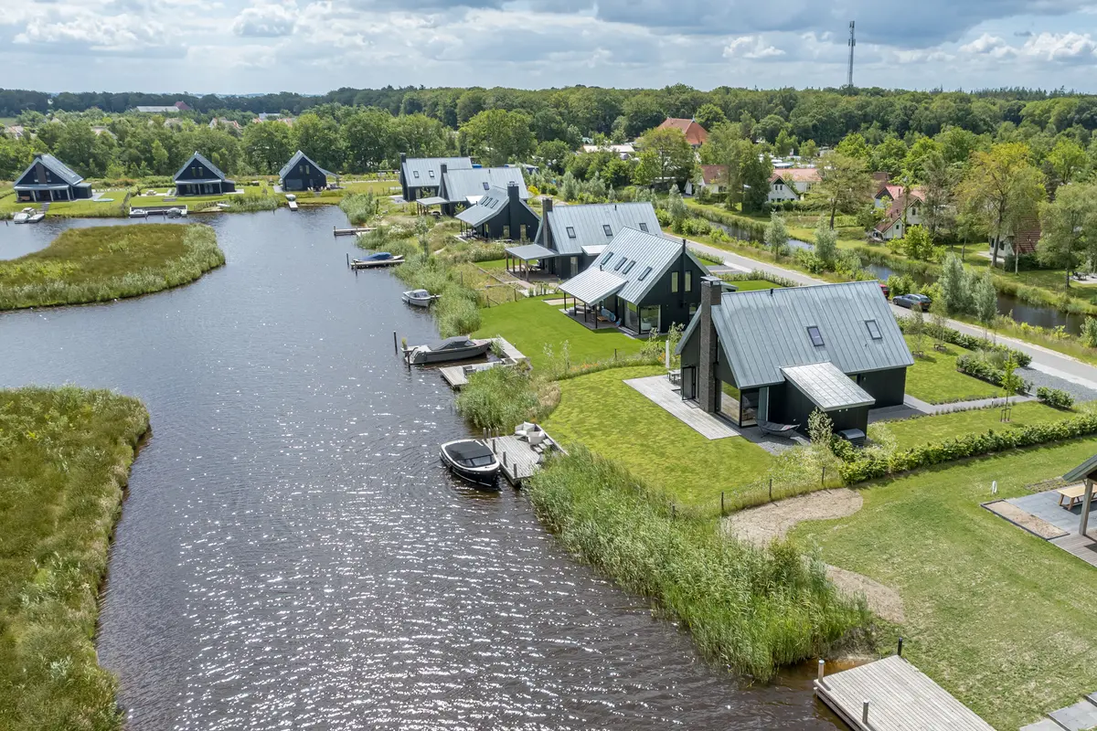 Luchtfoto van vrijstaande woningen met eigen aanlegsteigers langs een brede vaart